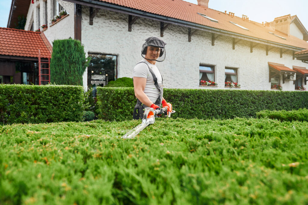 man in uniform, glasses and gloves pruning bushes at garden
